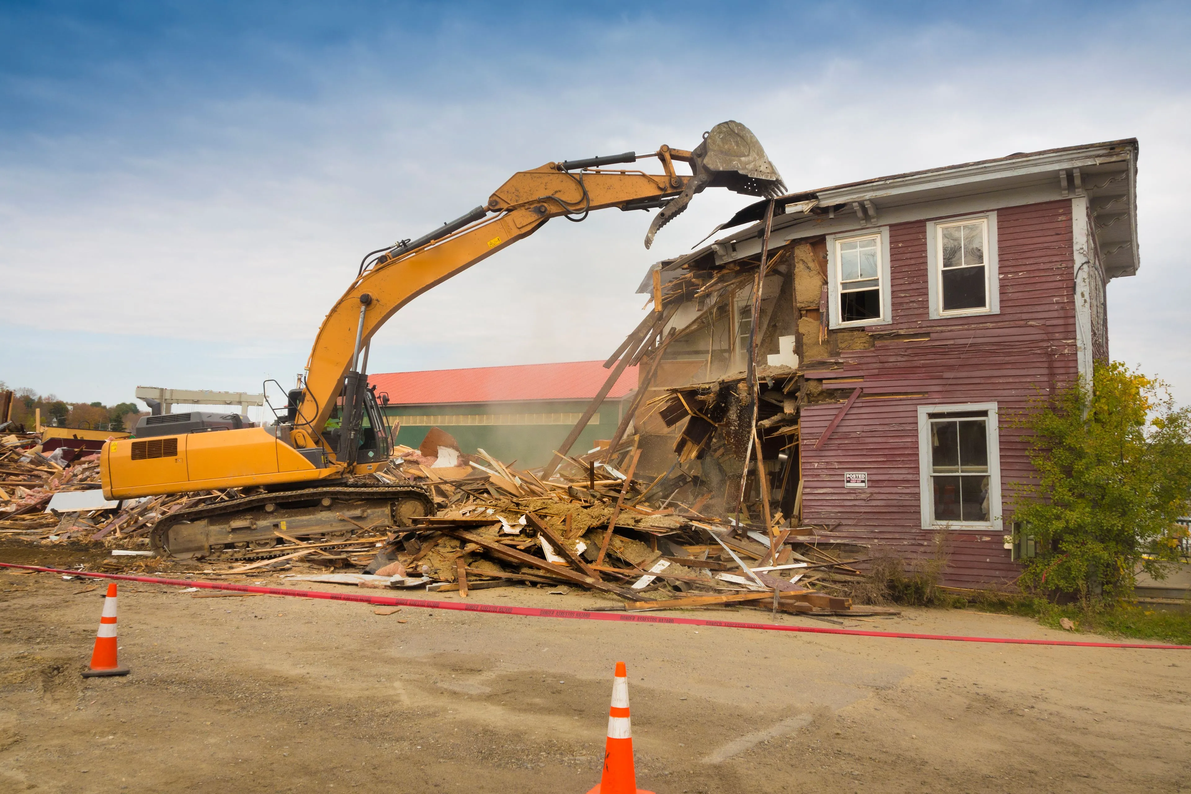 Large yellow excavator performing a full structural teardown of a residential home in Dallas, Texas.