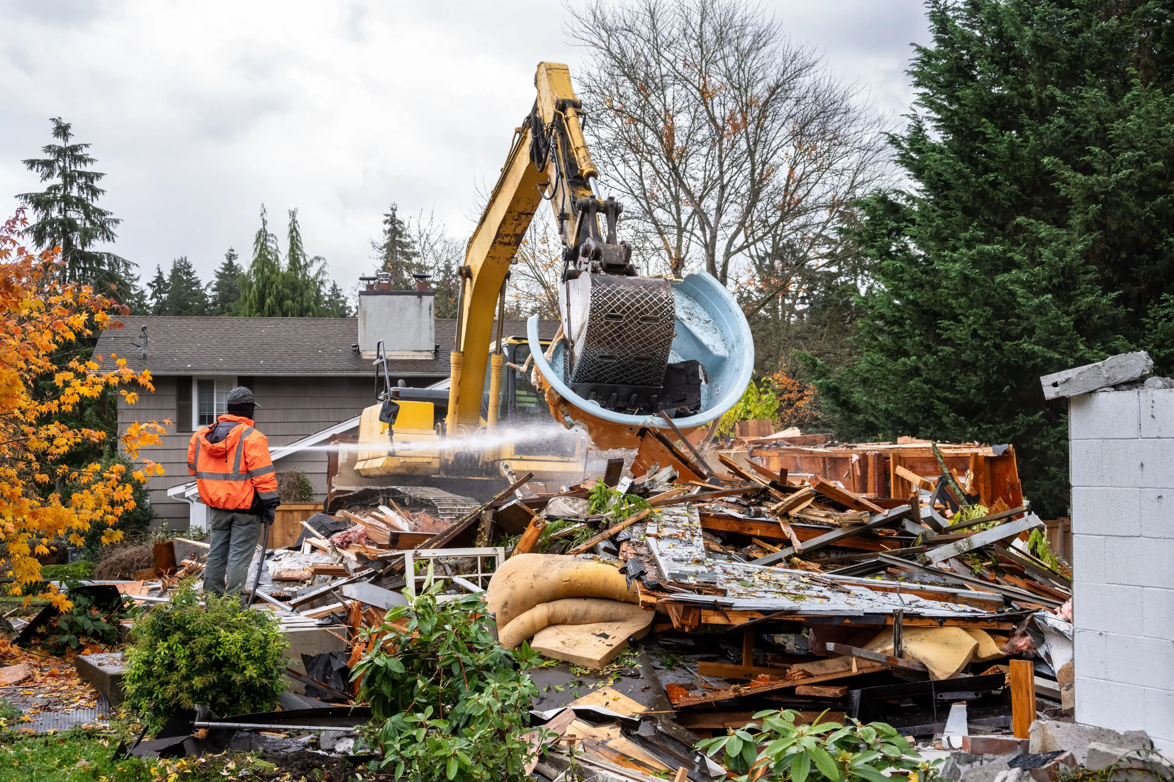 Professional excavator tearing down a residential structure in Dallas with water-based dust suppression